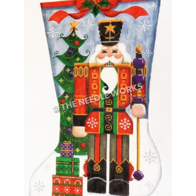 blue and white stocking with nutcracker wearing red and green suit with black and gold trim holding a gold and purple staff standing in front of a Christmas tree in the snow with gifts at the toe
